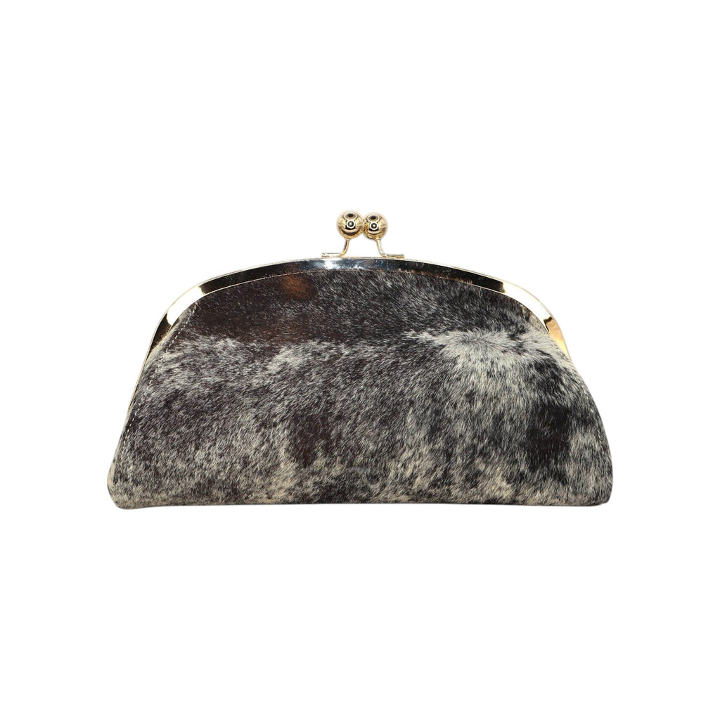 Clutch Jesalin Aluna de piel bovina con estampado de vaca, marco metálico dorado y cierre tipo kiss lock.