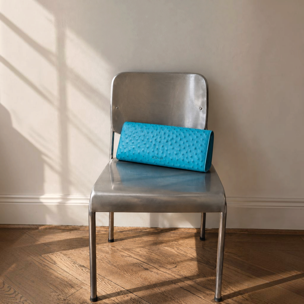 Jesalin Riga clutch in aqua bovine leather with ostrich-style embossing, resting on a metallic chair.